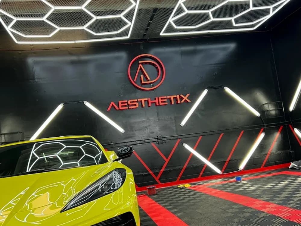 Backlit wall logo in a car detailing showroom above a yellow sports car