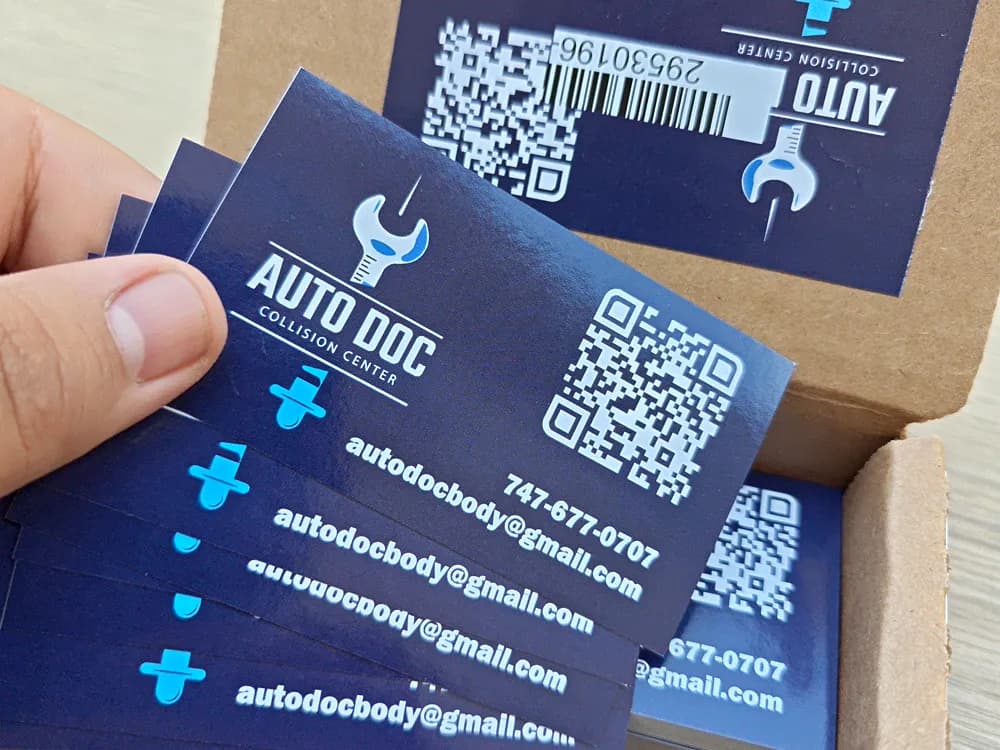 Navy business cards with a wrench logo and QR code, fanned out over the box they shipped in