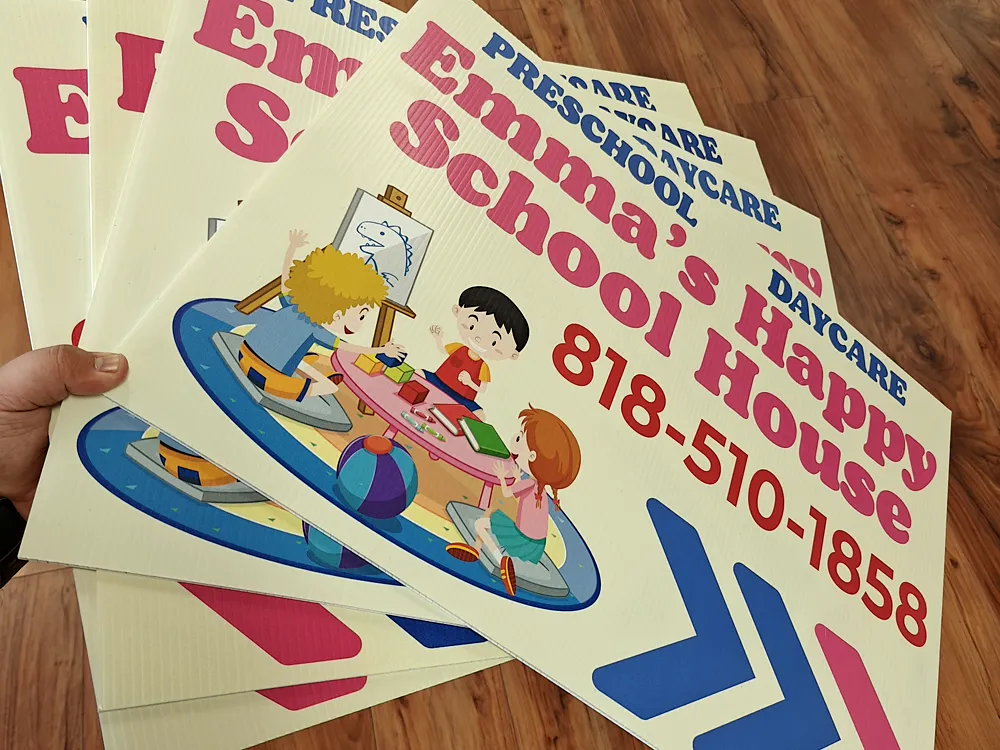 Stack of colourful printed daycare directional signs with arrows and a phone number