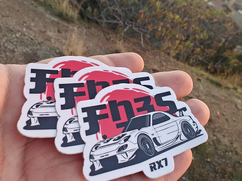 Hand holding contour-cut vinyl stickers illustrating an RX-7 sports car