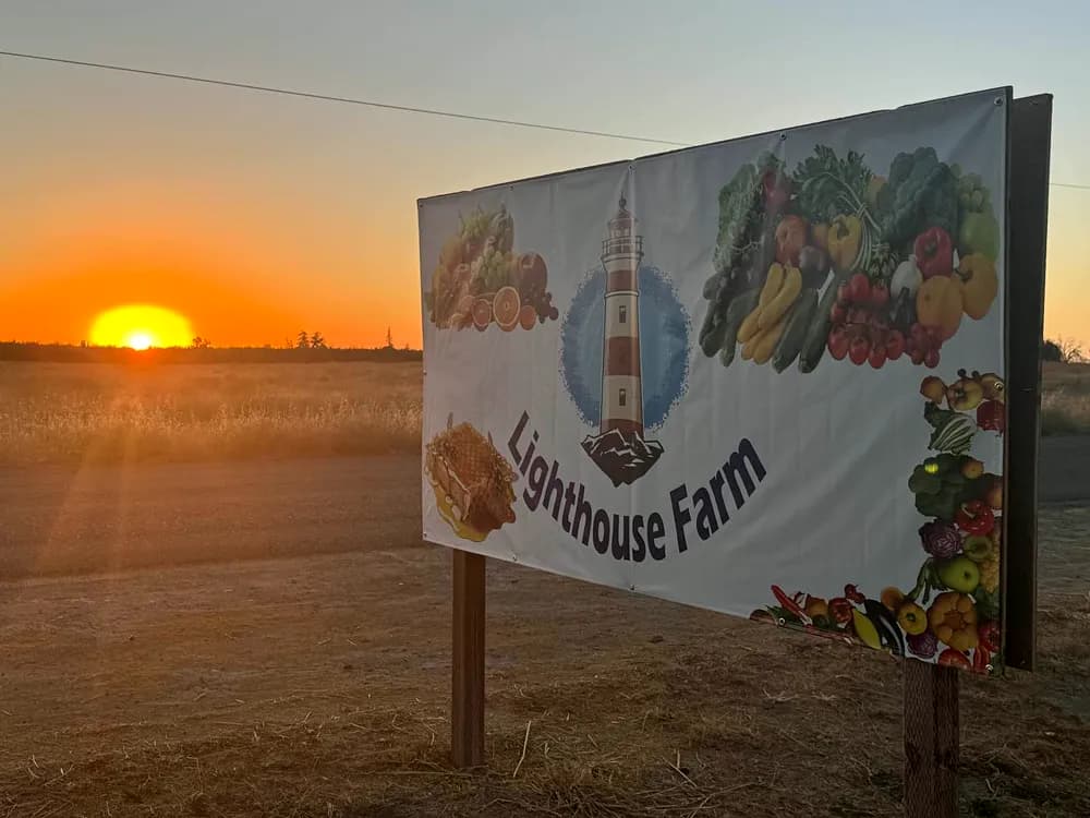 Large roadside farm-stand sign photographed against a sunset