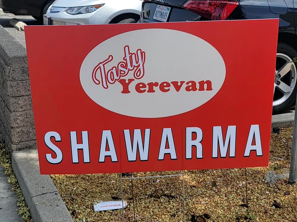Red corrugated plastic yard sign reading Tasty Yerevan Shawarma