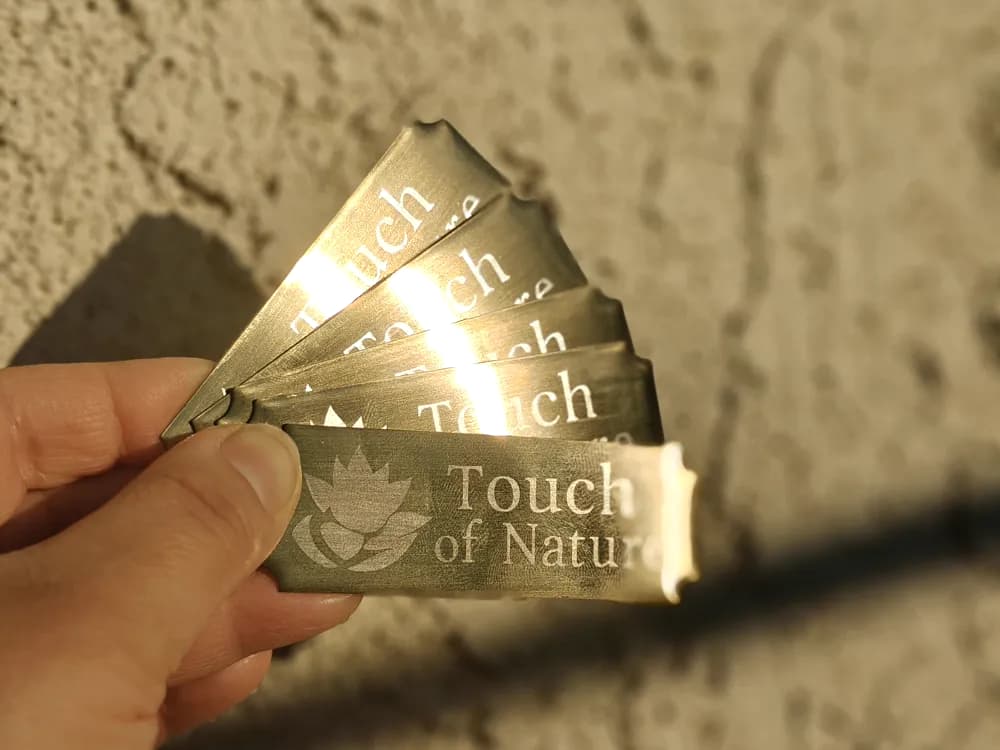 Fan of engraved brushed gold metal tags reading Touch of Nature