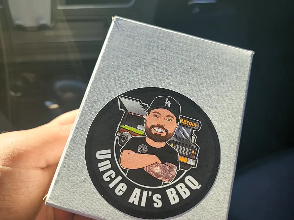 Circular die-cut card with an illustrated pitmaster logo for Uncle Al’s BBQ