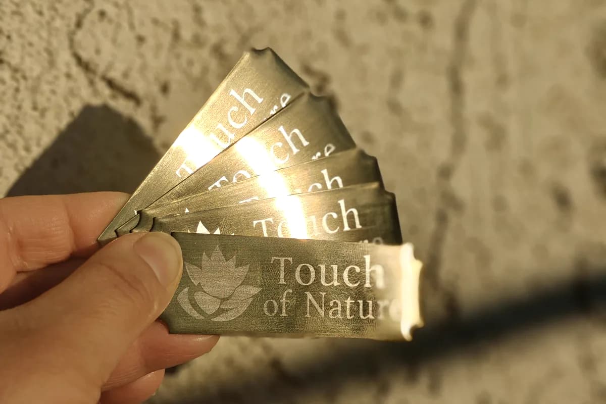 Fan of engraved brushed gold metal tags reading Touch of Nature