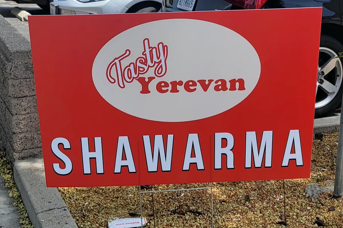 Red corrugated yard sign reading Tasty Yerevan Shawarma staked at a roadside