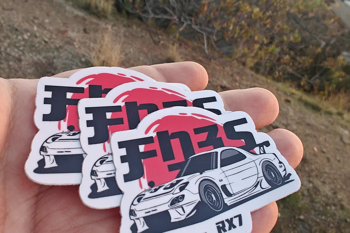 Hand holding a stack of die-cut vinyl car stickers illustrating an RX-7